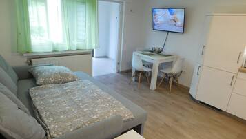 Ein modernes, gut beleuchtetes Zimmer mit einem grauen Sofa, einem kleinen weißen Tisch und einem an der Wand befestigten Fernseher.