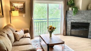 A living room with a sofa, a coffee table with a vase of flowers, a fireplace, and a balcony with curtains. - Downtown Condo-Walk Everywhere | Dog-Friendly (Breckenridge)