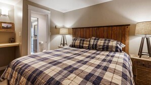 A bedroom with a large bed, wooden headboard, two bedside lamps, and a door leading to a bathroom. - Downtown Condo-Walk Everywhere | Dog-Friendly (Breckenridge)