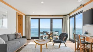 A modern living room with a sofa, a coffee table, a chair, a desk, and a large window with a view of the sea. - SA Beach Suite 6 by Stay Awhile Villas (Malibu)