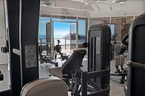 A gym with exercise equipment, large windows, and a view of the ocean.