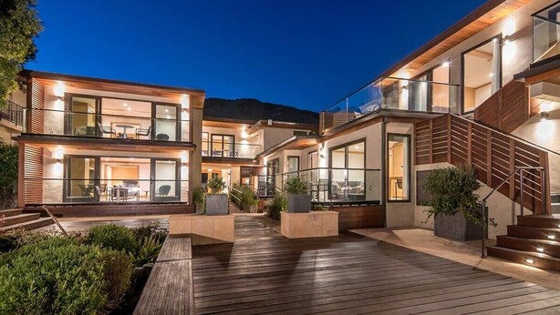 Una casa moderna de varios pisos con terraza de madera, mobiliario exterior y ventanas amplias.
