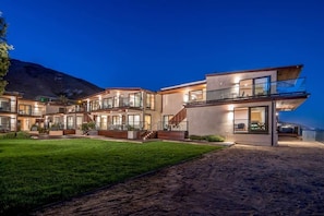 A modern multi-story building with large windows, a well-maintained lawn, and a mountain in the background.