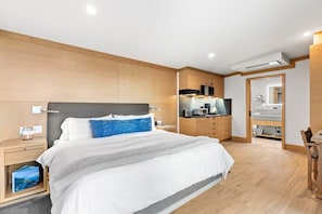 Une chambre d’hôtel moderne dotée d’un grand lit, d’une petite table de chevet, d’un coin cuisine intégré et d’une salle de bain avec un miroir.