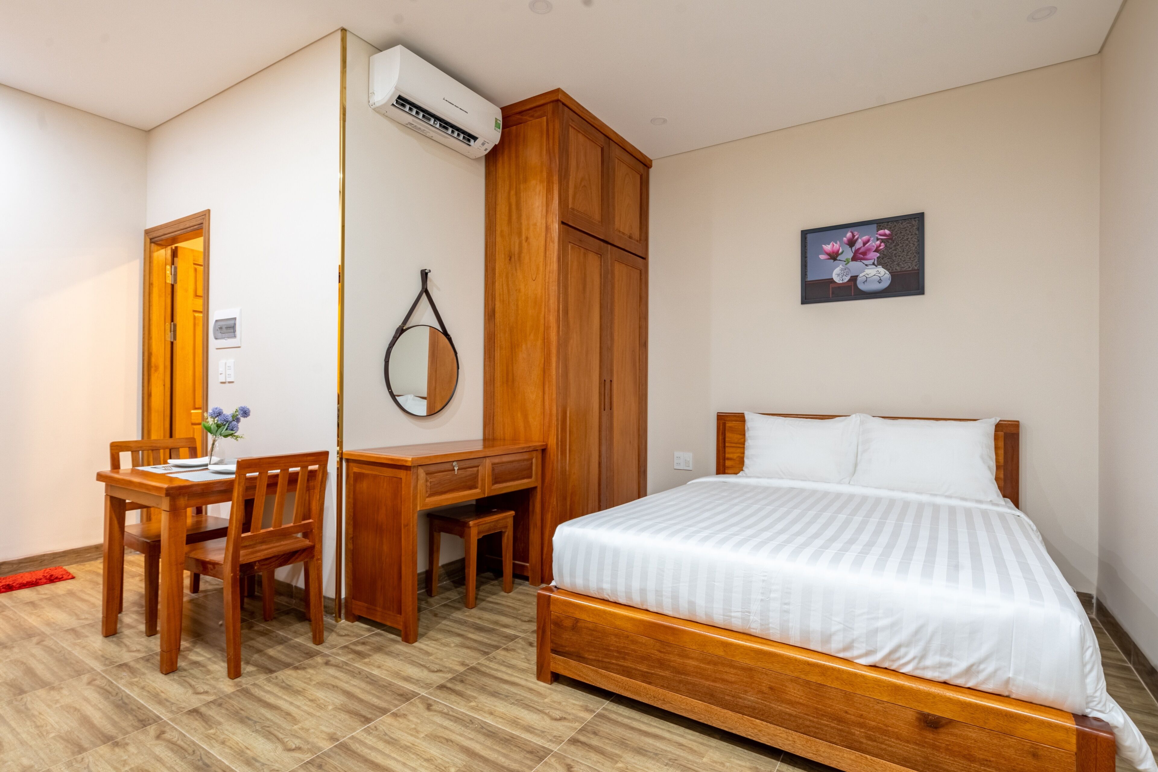 A bedroom with a wooden bed, a desk with a chair, a wardrobe, and a wall-mounted air conditioner.
