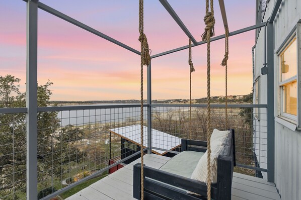 Un balcon doté d’un fauteuil suspendu, offrant une vue sur une étendue d’eau et un paysage lointain.