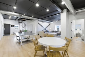 A spacious living area with a ping pong table, a round dining table, and a staircase leading to an upper level.