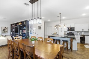 Une cuisine moderne avec des meubles blancs, une table à manger en bois et des luminaires suspendus.