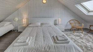 A bedroom with a sloped ceiling, a skylight, a large bed with pillows, two bedside tables with lamps, a wicker chair, and a fluffy rug. - Kerelen - Maison familiale avec jardin proche plage - Carantec (Carantec)