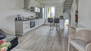 A modern kitchen with white cabinets, a dining area with a glass table and black chairs, and a staircase leading to another level. - Kerelen - Maison familiale avec jardin proche plage - Carantec (Carantec)