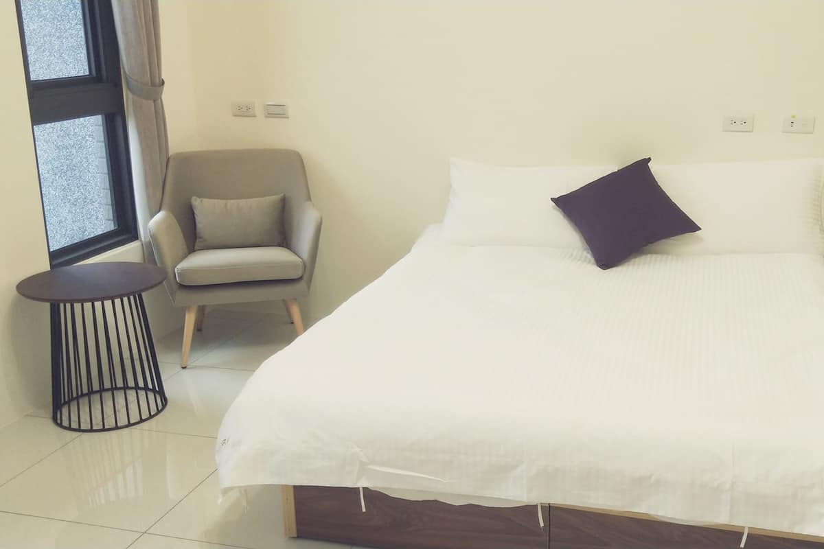 A neatly arranged bedroom with a bed, a chair, a bedside table, and a small round table.