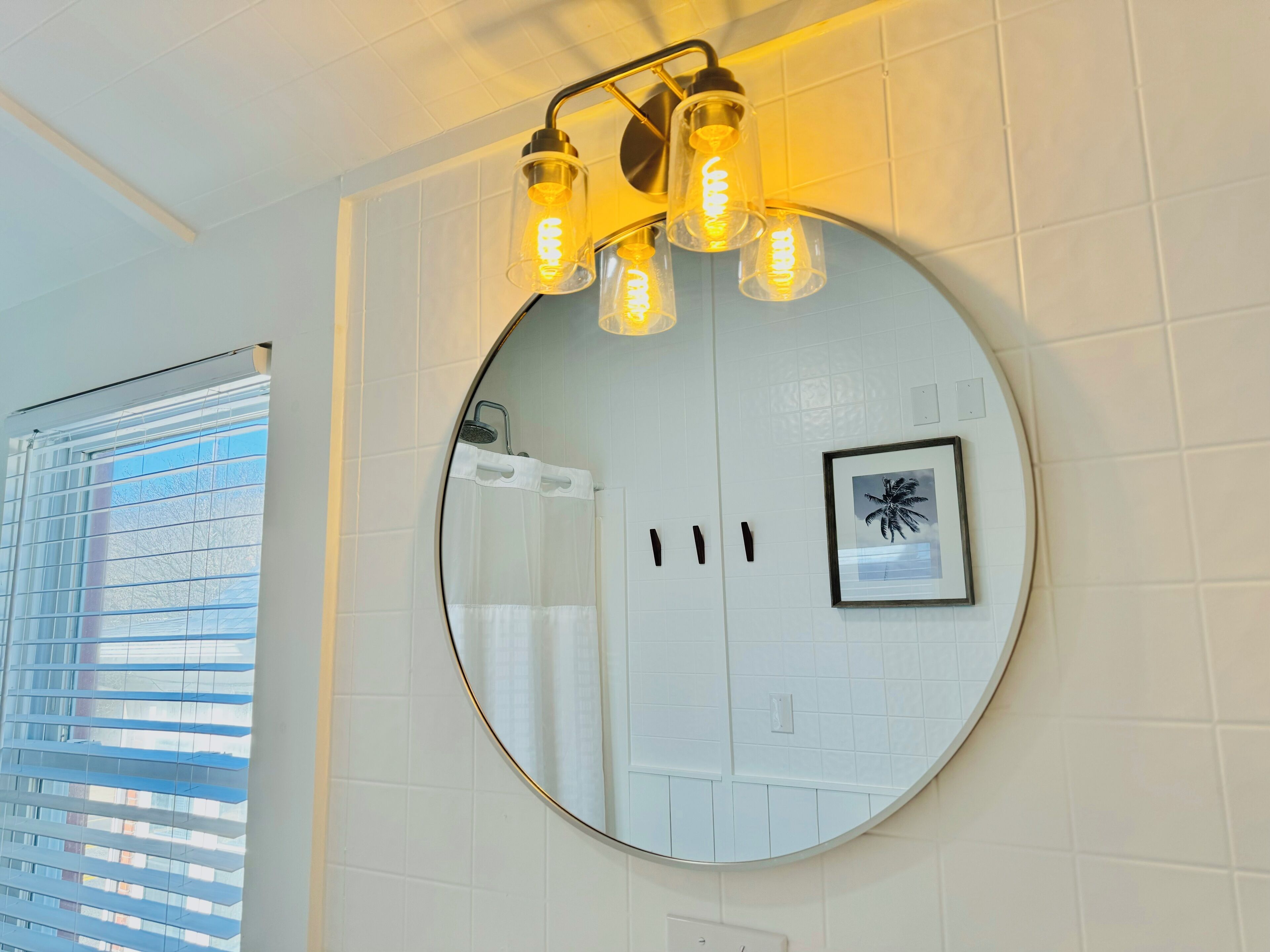 A bathroom with a round mirror, a framed picture, and a light fixture with exposed bulbs.