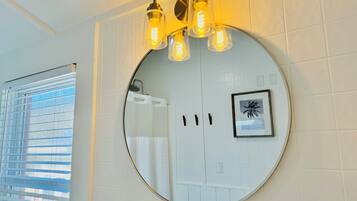 A bathroom with a round mirror, a framed picture, and a light fixture with exposed bulbs.