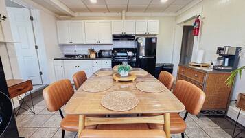 Un comedor con mesa de madera y sillas de cuero, armarios blancos, un refrigerador negro y una cafetera.
