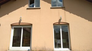 Ein zweistöckiges Gebäude mit einer beigen Fassade, zwei großen Fenstern mit weißen Rahmen und einem braunen Dach.
