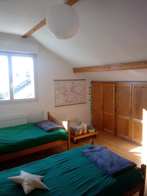 Une chambre avec deux lits, une armoire en bois, une carte accrochée au mur et une fenêtre donnant sur des immeubles.