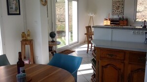 Ein Essbereich mit Holztisch und -stühlen, eine Küche mit Holzschränken und ein Blick durch eine Glastür in einen Außenbereich.