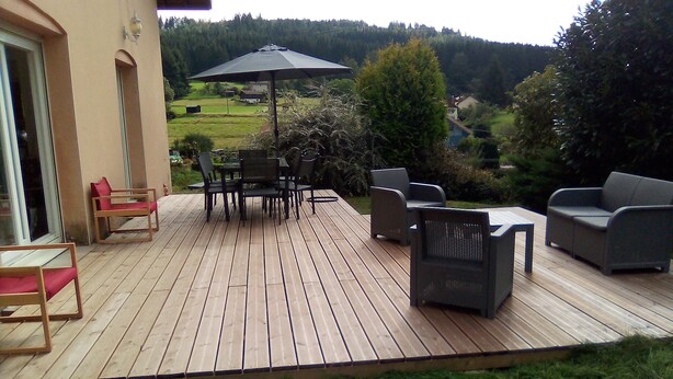 Eine Holzterrasse mit Gartenmöbeln, darunter ein Tisch und Stühle, sowie ein großer Sonnenschirm.