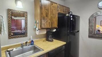 A kitchen with wooden cabinets, a black refrigerator, a coffee maker, and a sink.