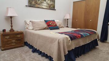 Une chambre à coucher avec un lit, deux lampes de chevet, une commode en bois, un tableau au mur et une armoire.
