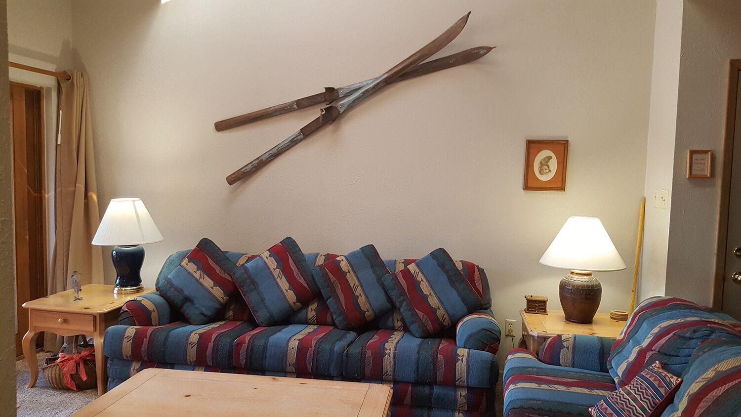 Un salon comprenant un canapé, deux tables d’appoint avec des lampes, une table basse en bois et un grand objet en bois accroché au mur.