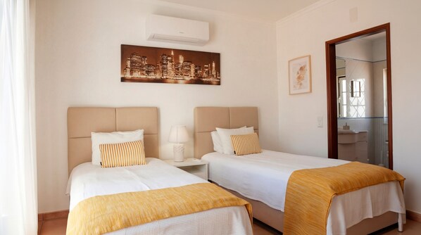 A hotel room with two beds, a cityscape painting, a mirror, and a window.