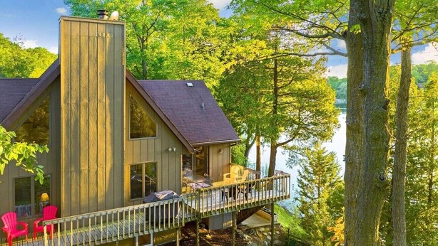 A cabin with a deck overlooking a lake, surrounded by trees. - Walk to Road America Races. Enjoy the lake frontage and fishing and kayaking. (Plymouth)