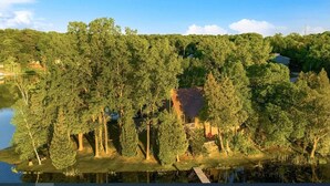 A lakeside property with a house surrounded by dense trees, a dock, and a clear sky. - Walk to Road America Races. Enjoy the lake frontage and fishing and kayaking. (Plymouth)