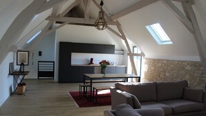 Um loft espaçoso com pé direito alto, vigas aparentes, cozinha e uma área de estar aconchegante com um tapete vermelho.