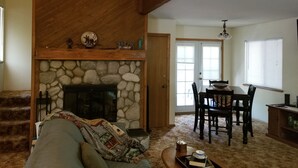 A cozy living room with a stone fireplace, a wooden ceiling, a dining area with a table and chairs, and a staircase leading to another level. - Somethings old, somethings new, clean and cozy just for you. (ArrowBear)