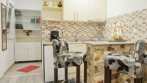 Una cocina compacta con una isla de piedra, dos sillas estampadas, un tapete rojo y un armario blanco con espejo.