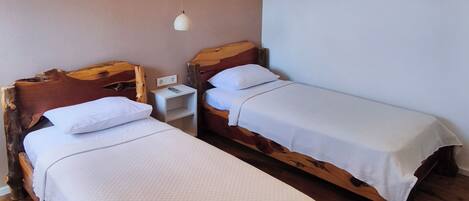 A room with two wooden beds, a white wall, a ceiling light, and an air conditioning unit.