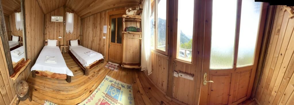Una cabaña de madera con dos camas individuales, un baño pequeño y un ventanal con vistas a la montaña.