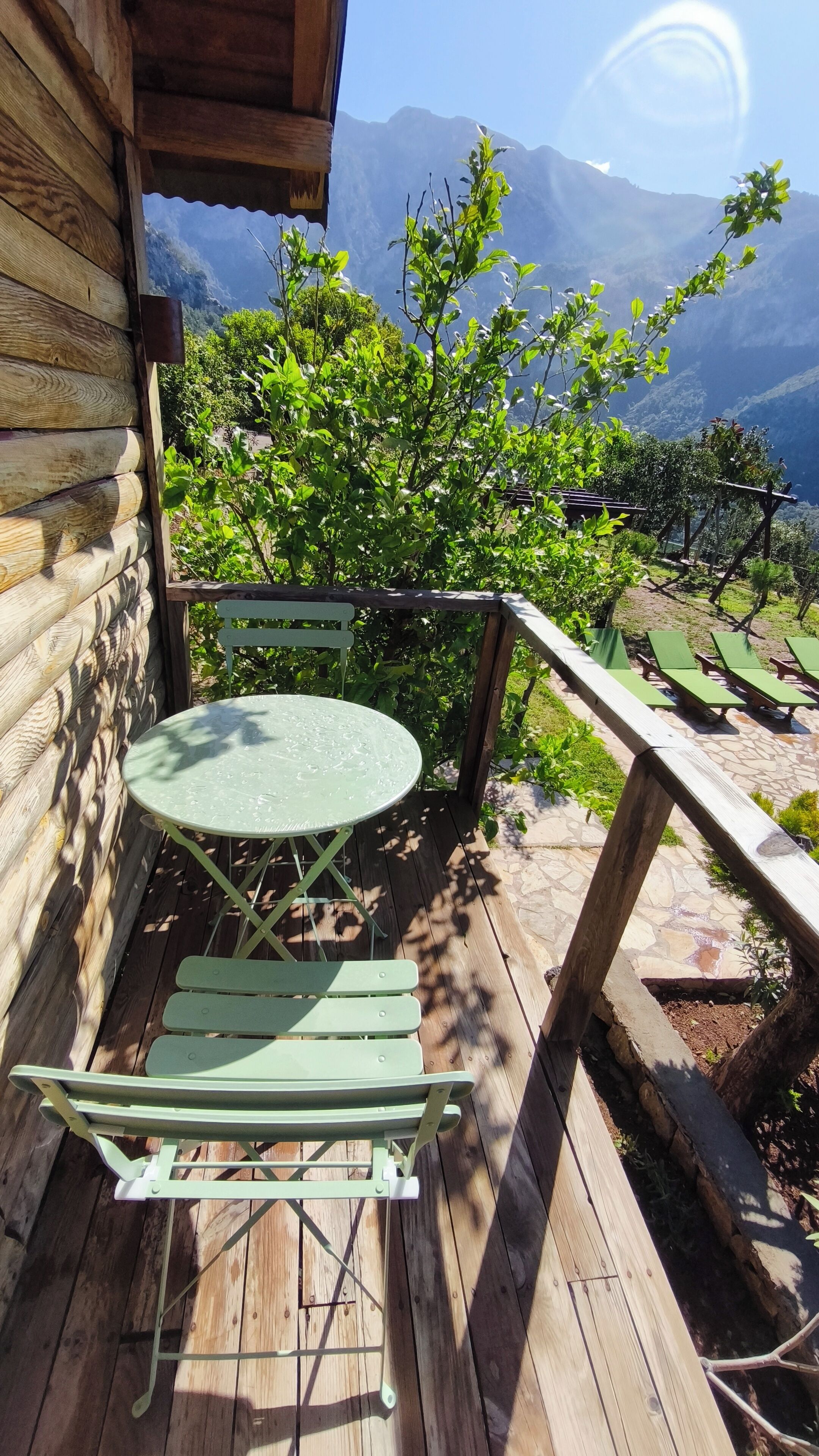 A wooden deck with a table and chairs, overlooking a mountainous landscape.