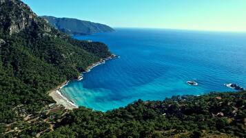 A coastal landscape with a clear view of the sea, a beach, and a mountainous backdrop.