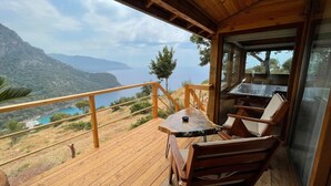 Una terraza de madera con una mesa y sillas, con vistas a un paisaje costero pintoresco con montañas y un mar azul cristalino.