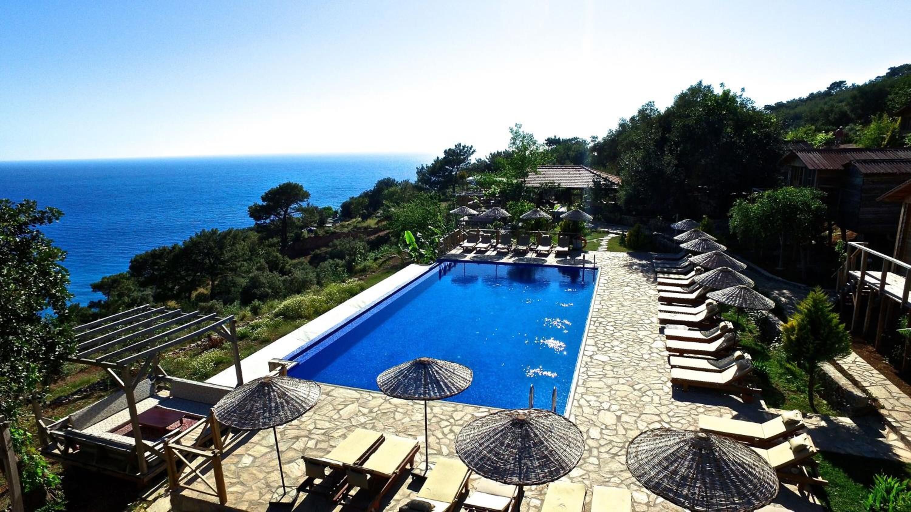 Ein rechteckiger Pool mit Liegestühlen und Sonnenschirmen, umgeben von Grün und mit Blick auf das Meer.