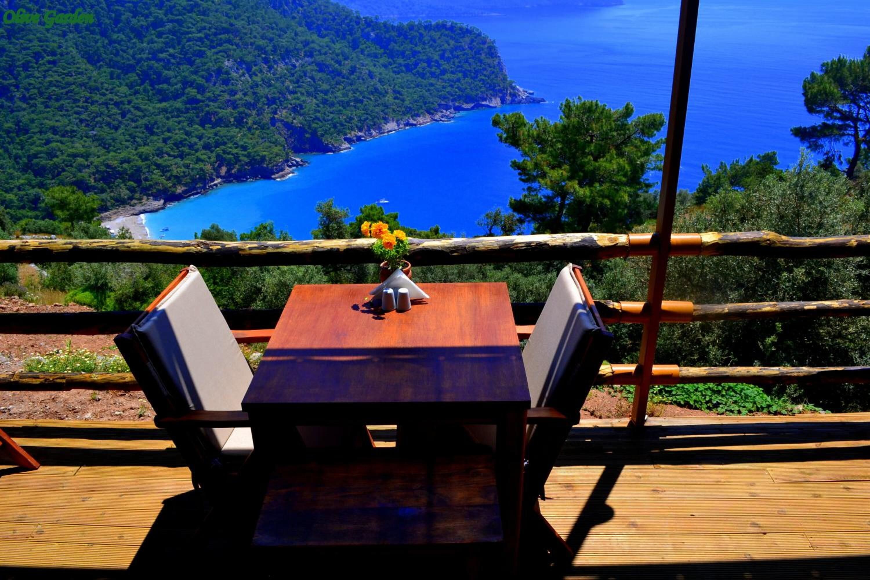 A wooden deck with a table and chairs overlooking a coastal landscape.