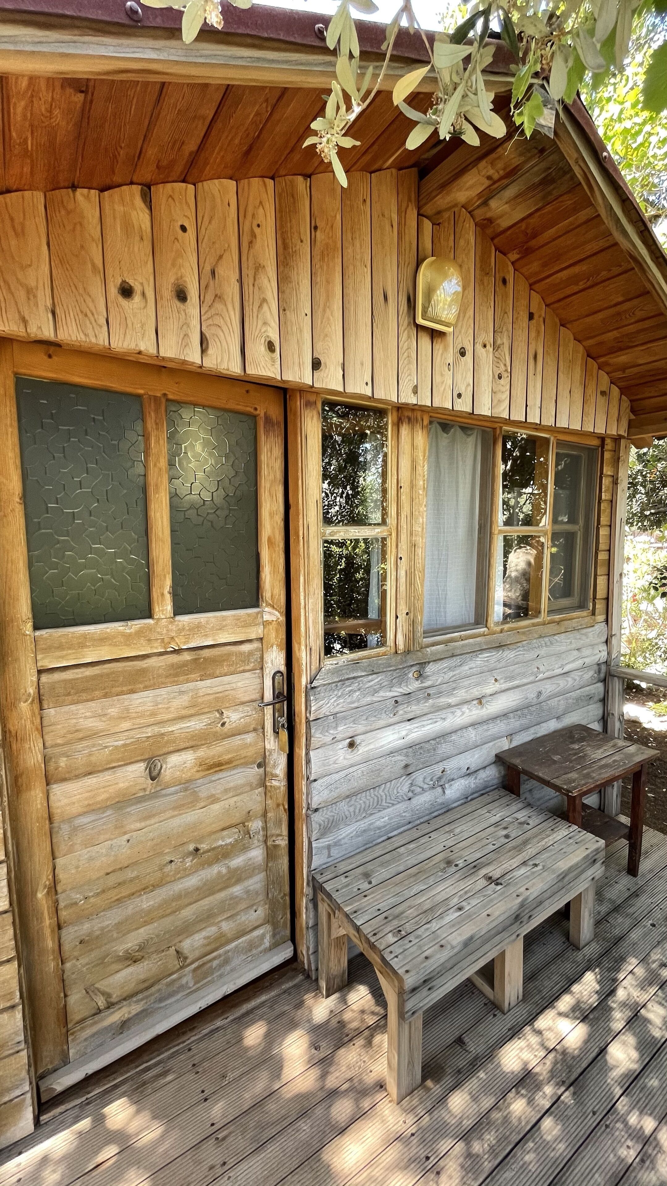 A wooden cabin with a porch, large windows, and a bench.
