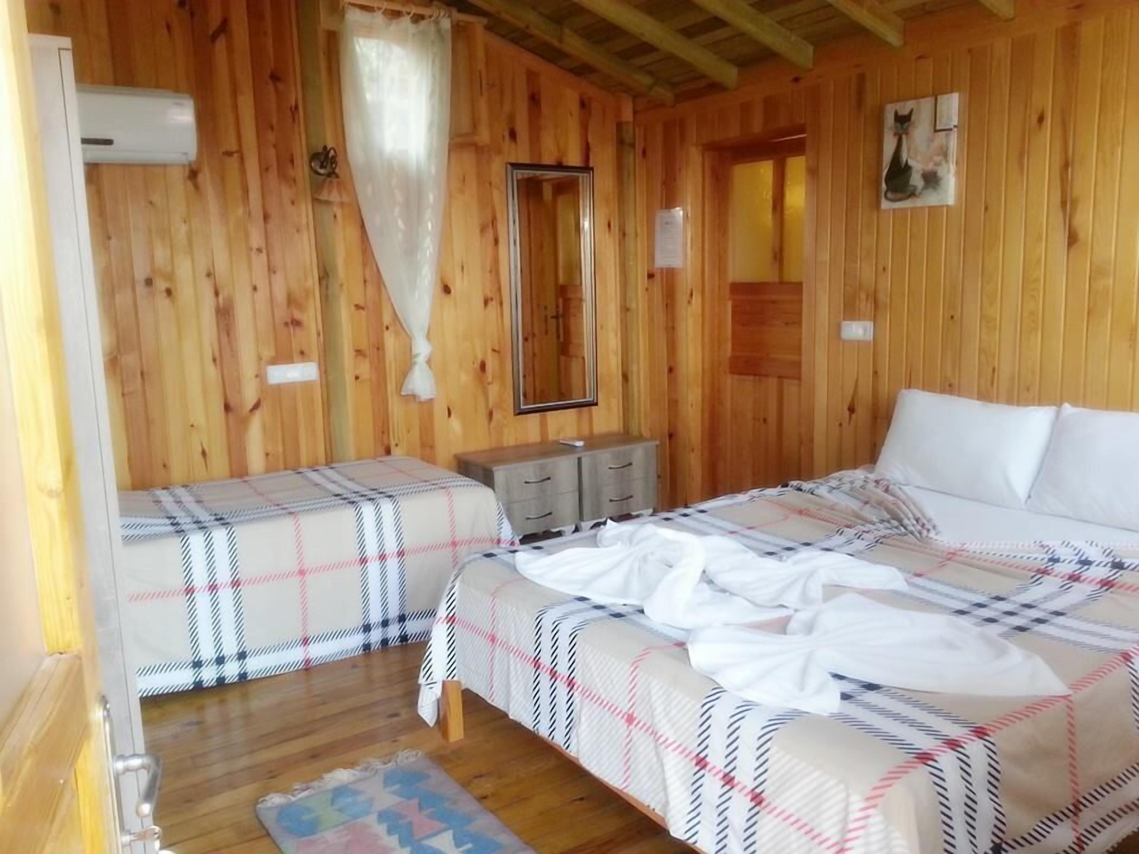 A wooden cabin bedroom with two beds, a dresser, a mirror, and a window with curtains.