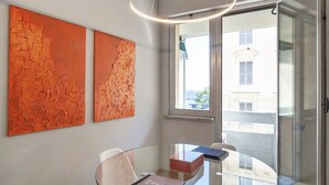 A modern room with a glass table, two abstract paintings, a ceiling light, and a view through a glass door. - Suite Blu a Genova by Wonderful Italy (Genova)