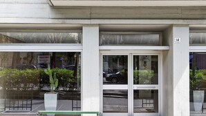 A building entrance with a glass door and windows, a green bench outside, and a potted plant in the foreground. - Suite Blu a Genova by Wonderful Italy (Genova)