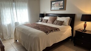 Une chambre à coucher bien rangée, avec un lit, des tables de chevet, un ventilateur de plafond et un tableau encadré au mur.