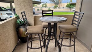 Une terrasse avec une table ronde et quatre chaises, un pot de fleurs et une vue sur la rue.