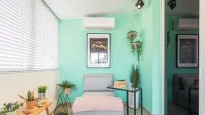 Una habitación con una pared verde azulado, una cama con cabecera gris, una mesita con una planta y un cuadro enmarcado en la pared.