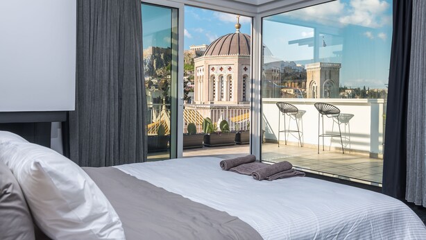 Habitación de hotel moderna con una cama grande, un balcón con sillas y vistas a un edificio histórico.