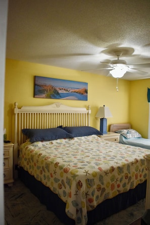 A bedroom with a bed, a ceiling fan, a nightstand, a lamp, and a painting on the wall. - 3rd Row-Only Steps Away from Paradise (Ocean Isle Beach)