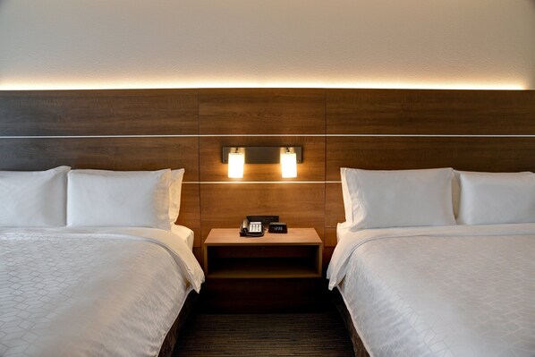 Habitación de hotel con dos camas, cabecero de madera, lámparas de noche, mesitas de noche con teléfono y reloj, y piso alfombrado.