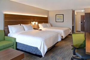 A hotel room with two beds, a green armchair, a desk, and a wooden headboard.