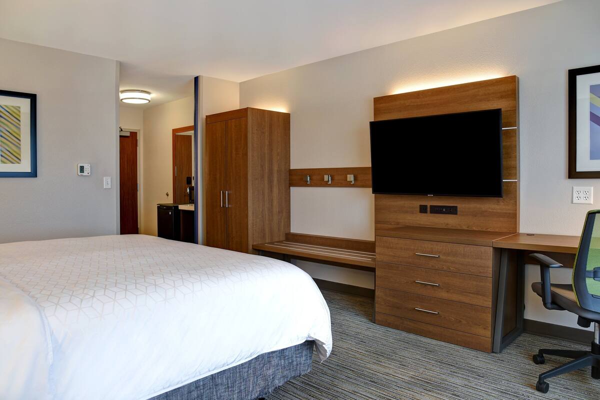 A hotel room with a large bed, a wooden desk, a flat-screen TV, and a chair.